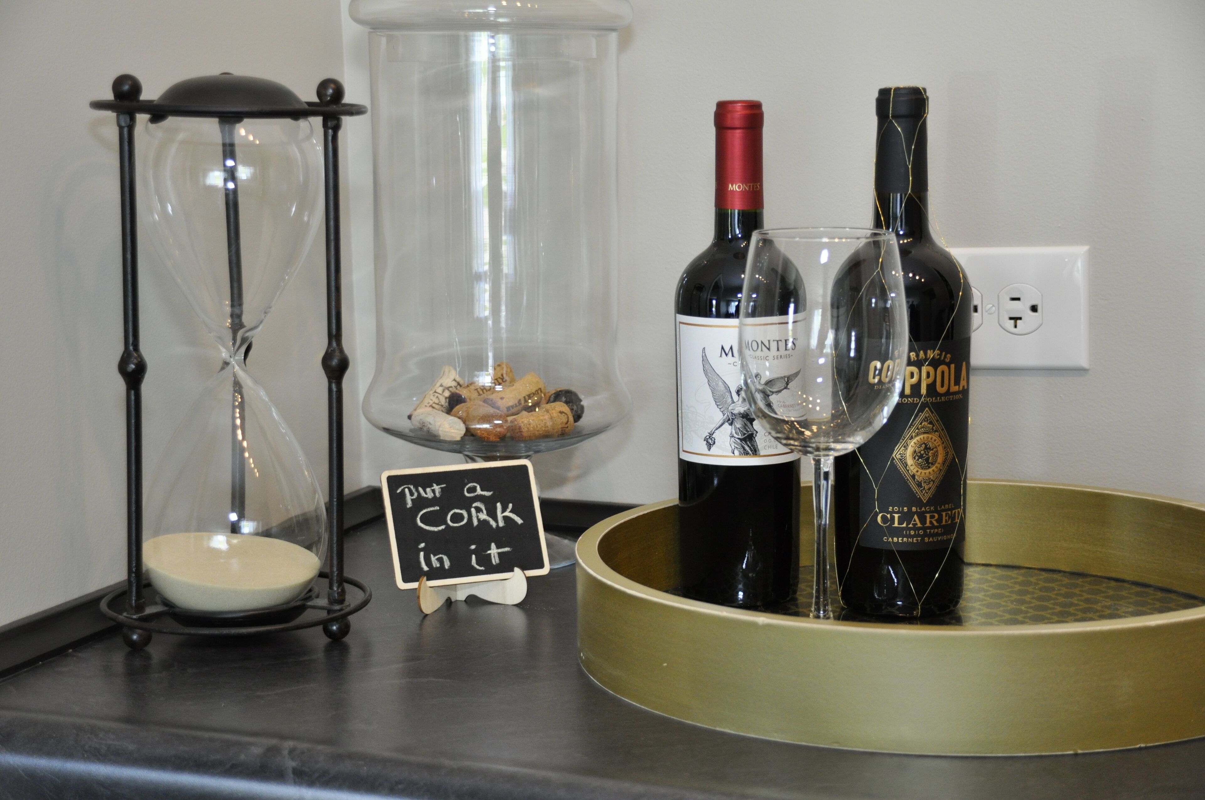 A wine display with bottles and a glass, a cork holder, and a sign.