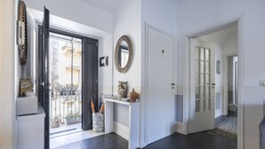 A hallway with a door leading to a balcony, a white console table with decorative items, and a large mirror on the wall.