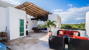 A rooftop terrace with a wooden pergola, a dining area with a table and chairs, a red sofa, and a potted palm tree. - Spectacular two level penthouse 850' to the beach and 1.5 blocks to 5th Ave. (Playa Del Carmen)