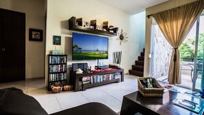 A living room with a TV, bookshelves, a coffee table, and a view of the outdoors. - Spectacular two level penthouse 850' to the beach and 1.5 blocks to 5th Ave. (Playa Del Carmen)