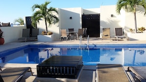 A swimming pool with lounge chairs and a table, surrounded by white walls and palm trees. - Spectacular two level penthouse 850' to the beach and 1.5 blocks to 5th Ave. (Playa Del Carmen)