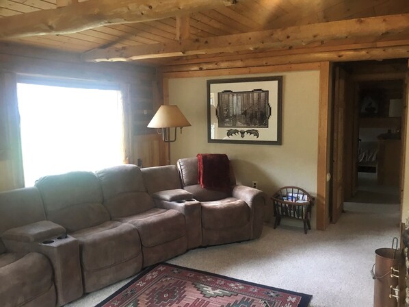 A cozy living room with a sectional sofa, a small armchair, a lamp, and a framed picture on the wall. - Creek front Log Cabin, Mountain Views, ATV Trails, hiking, fishing (Nathrop)