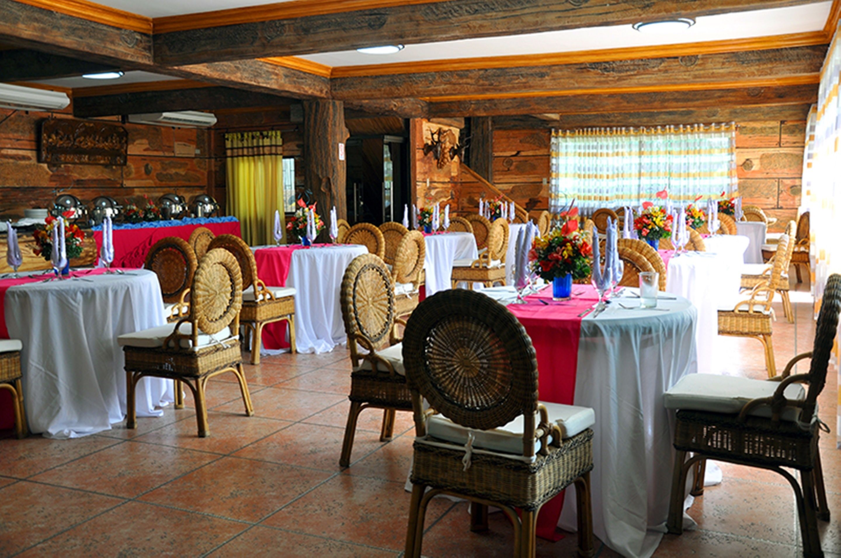 Un comedor con sillas y mesas de mimbre, paredes de madera y piso de baldosas.