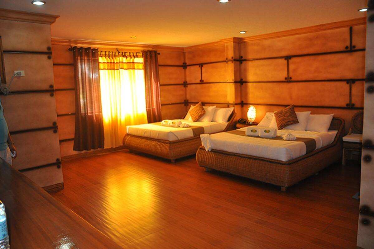 Une chambre d’hôtel avec deux lits simples, un plancher en bois, une grande fenêtre avec des rideaux et une tête de lit en bois.