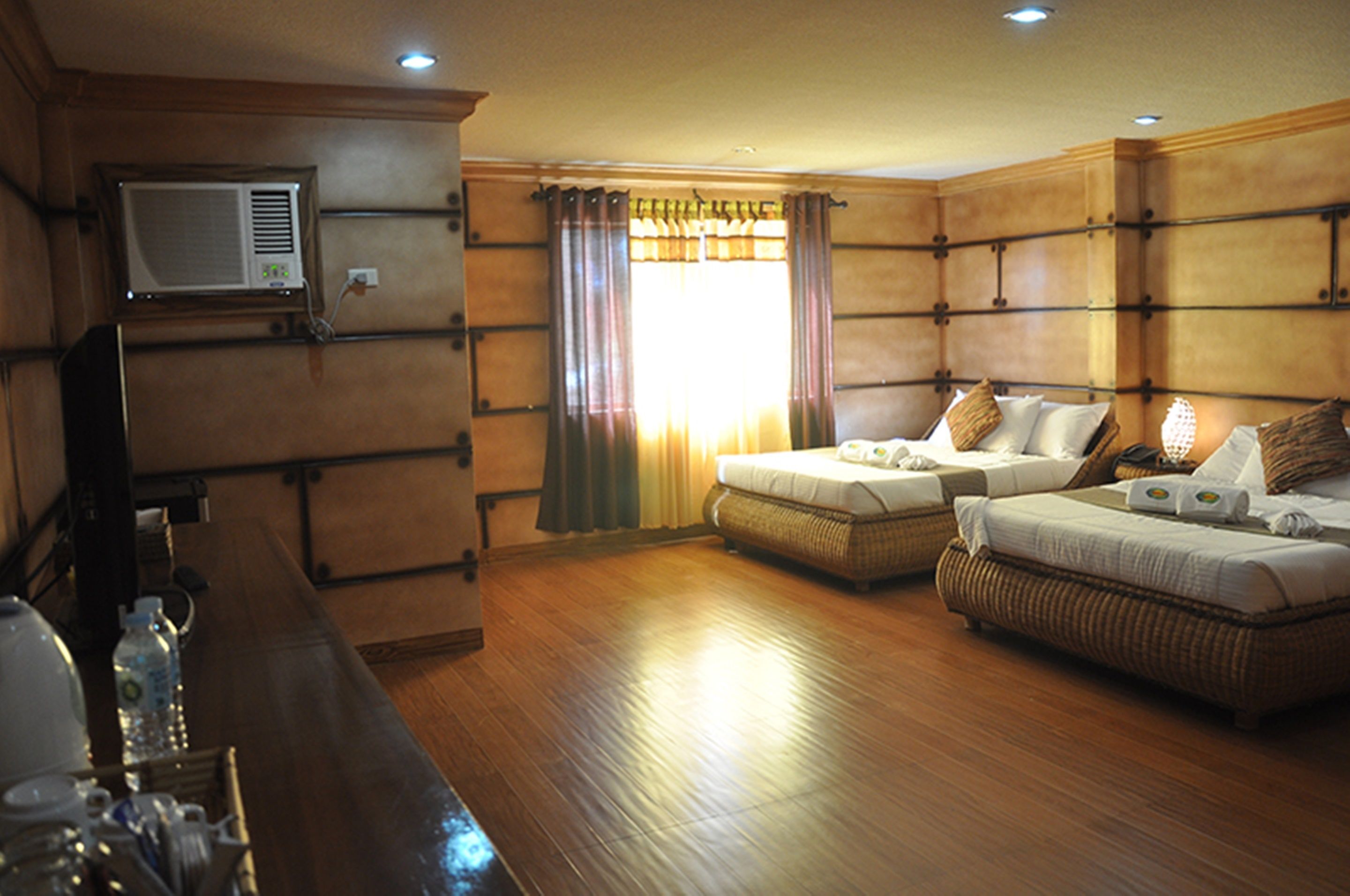 A hotel room with two beds, a television, a bar area, and a window with curtains.