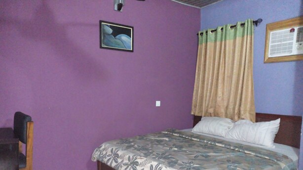 A bedroom with a bed, a chair, a purple wall, and a framed picture. - Solochus Hotel & Suites (Lagos)