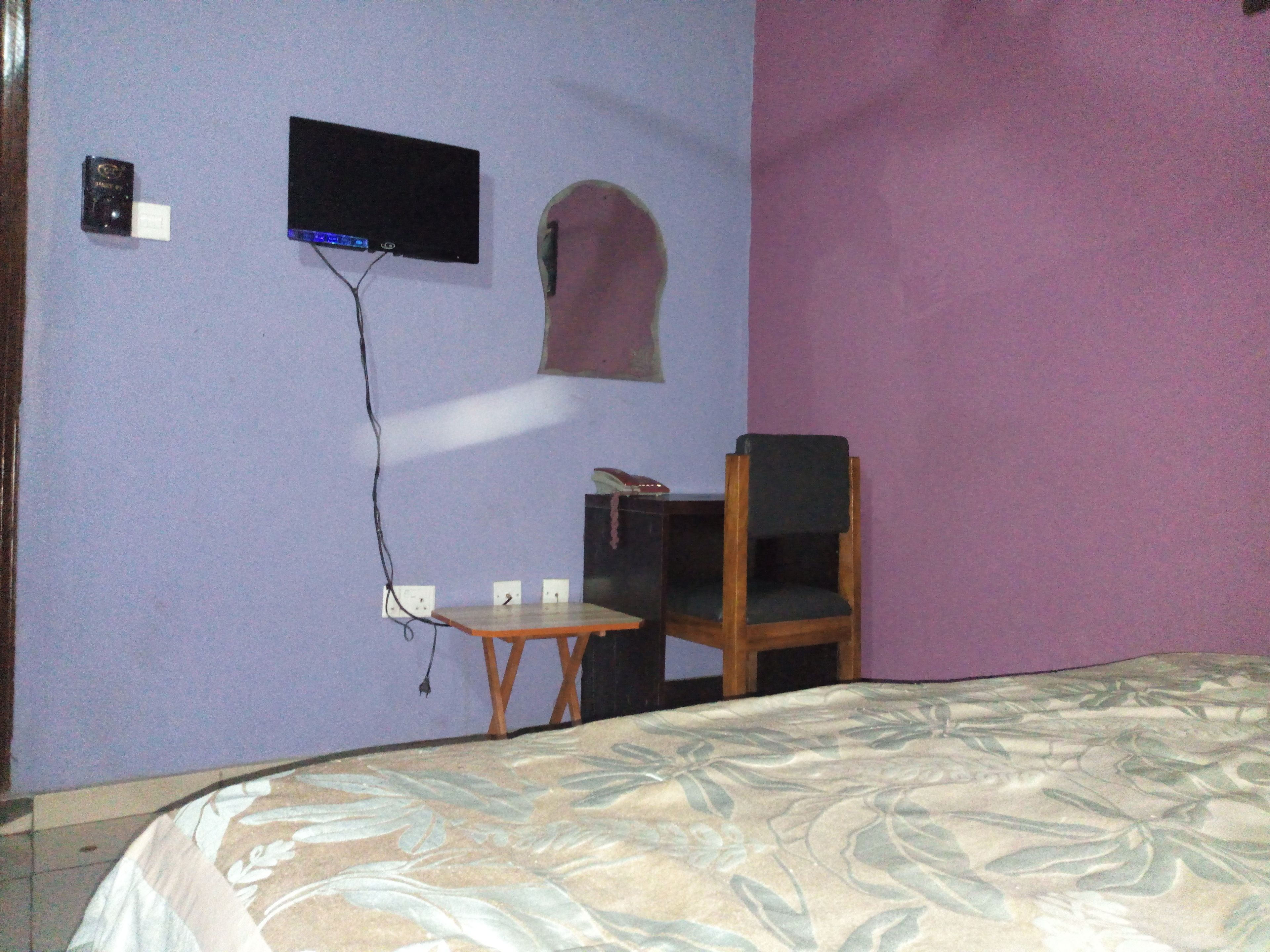 A bedroom with a bed, a desk, a chair, a television mounted on the wall, and a small table.