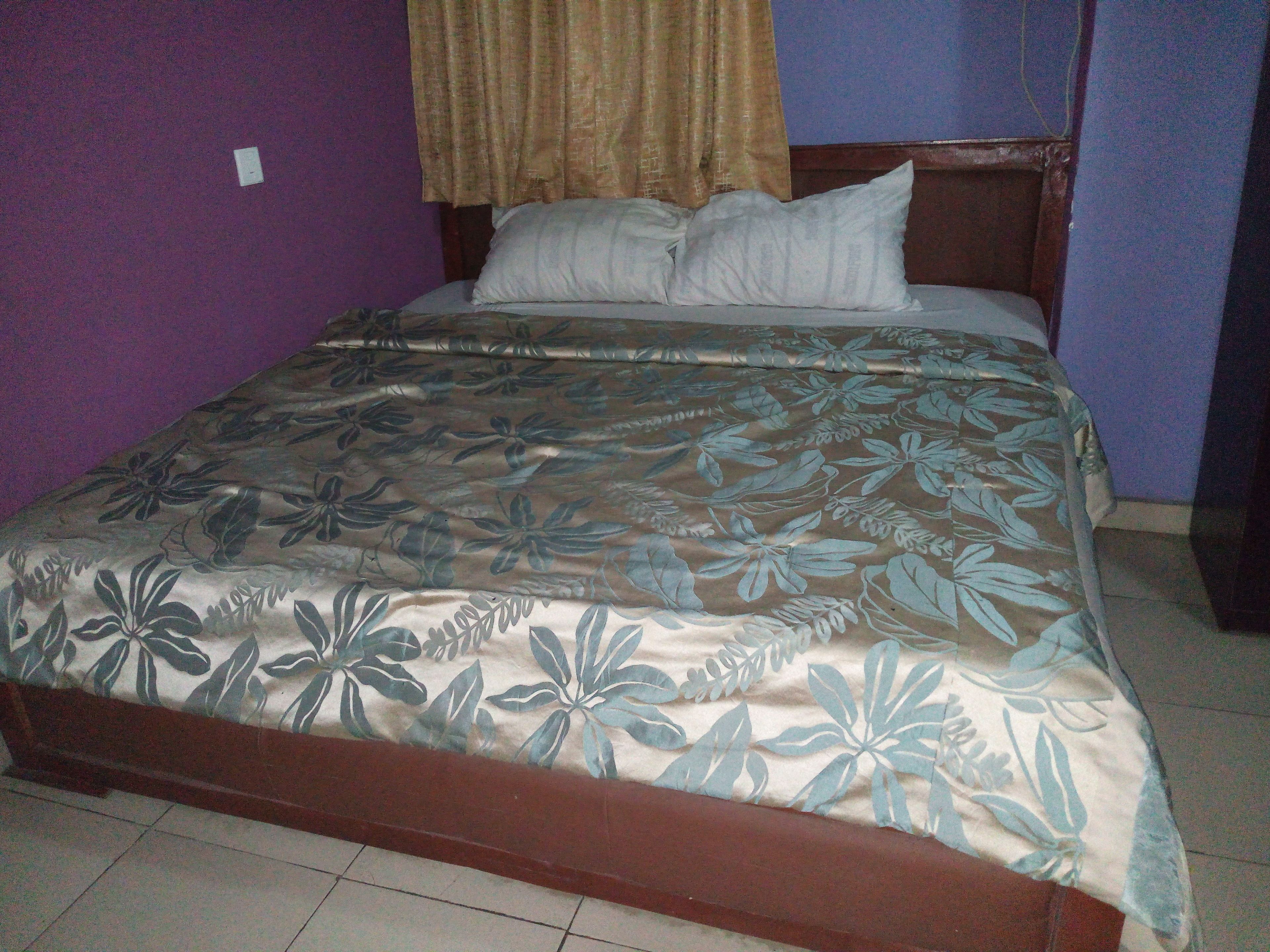 A bed with a floral-patterned bedspread, a wooden headboard, and a curtain.