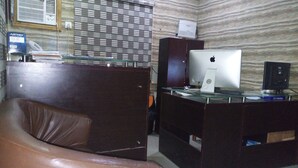 A room with a brown leather sofa, a wooden desk with an Apple iMac, a printer, and a glass partition. - Solochus Hotel & Suites (Lagos)
