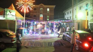 A hotel entrance with a large firework display, a covered outdoor seating area, and a building with a sign for 'Solo Chug Hotel & Lounge'. - Solochus Hotel & Suites (Lagos)