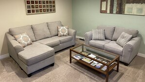 A living room with two grey sofas, a glass coffee table with magazines, and a wall with framed pictures. - Nederland Dual Level Apartment, Full Kitchen, No Cleaning Fee, Private! (Nederland)