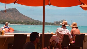 Un restaurant situé en bord de mer, avec une terrasse offrant une vue sur la plage et une montagne.