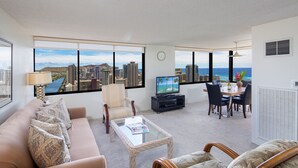 Un salon moderne avec vue sur la ville, comprenant un canapé, une table basse, un téléviseur et un coin repas avec des chaises et une table.