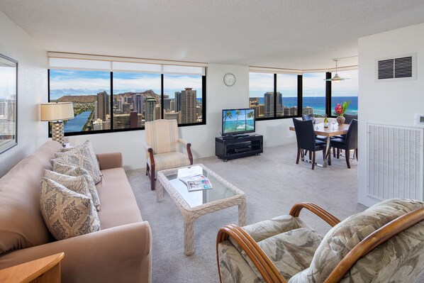 A modern living room with a city view, a sofa, a coffee table, a TV, and a dining area with chairs and a table.