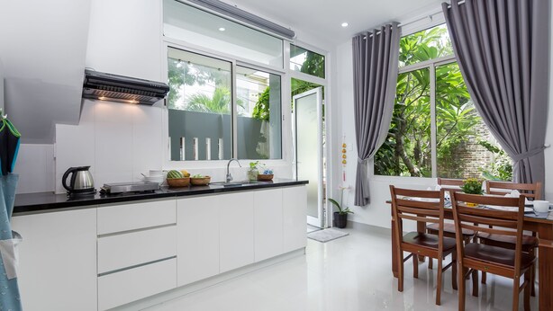 Een moderne keuken met witte kasten, een zwart aanrecht en een raam met grijze gordijnen.