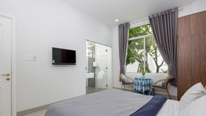 Een hotelkamer met een bed, een televisie, een raam met gordijnen, een stoel en een tafeltje met een vaas.