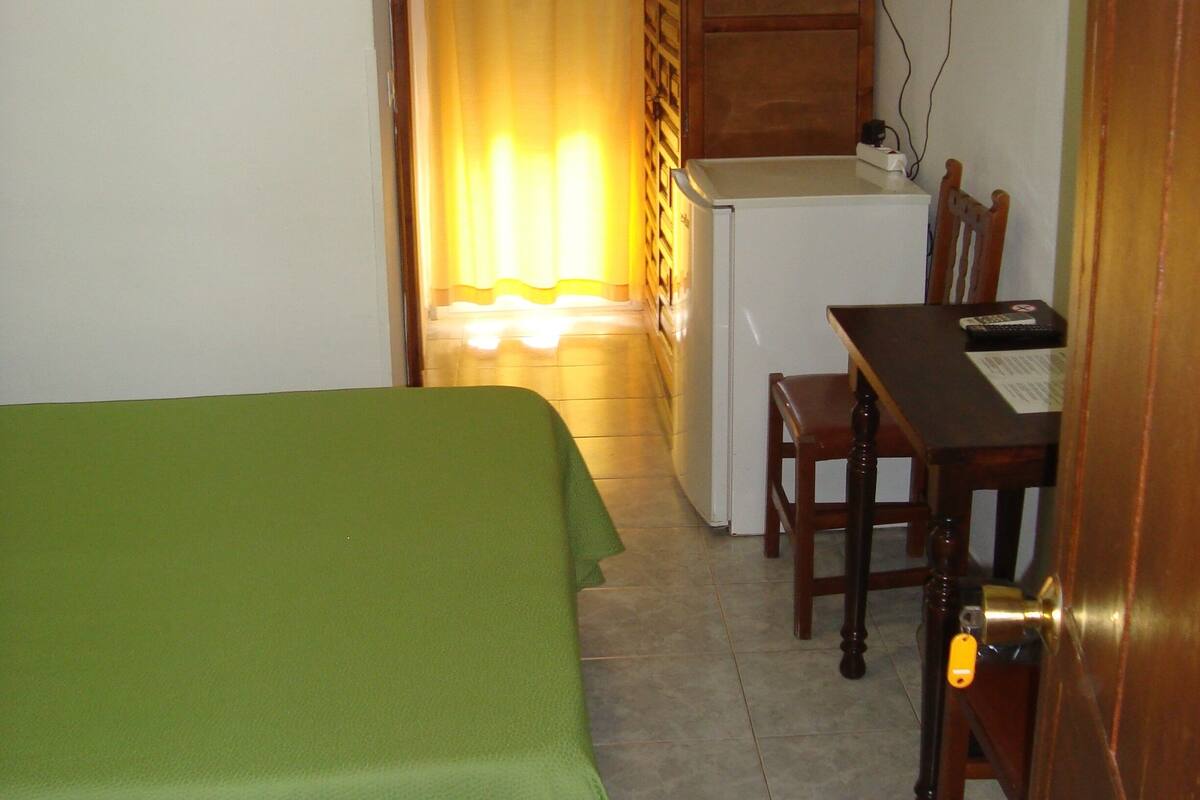 A room with a bed, a desk with a chair, a television, and a small refrigerator.