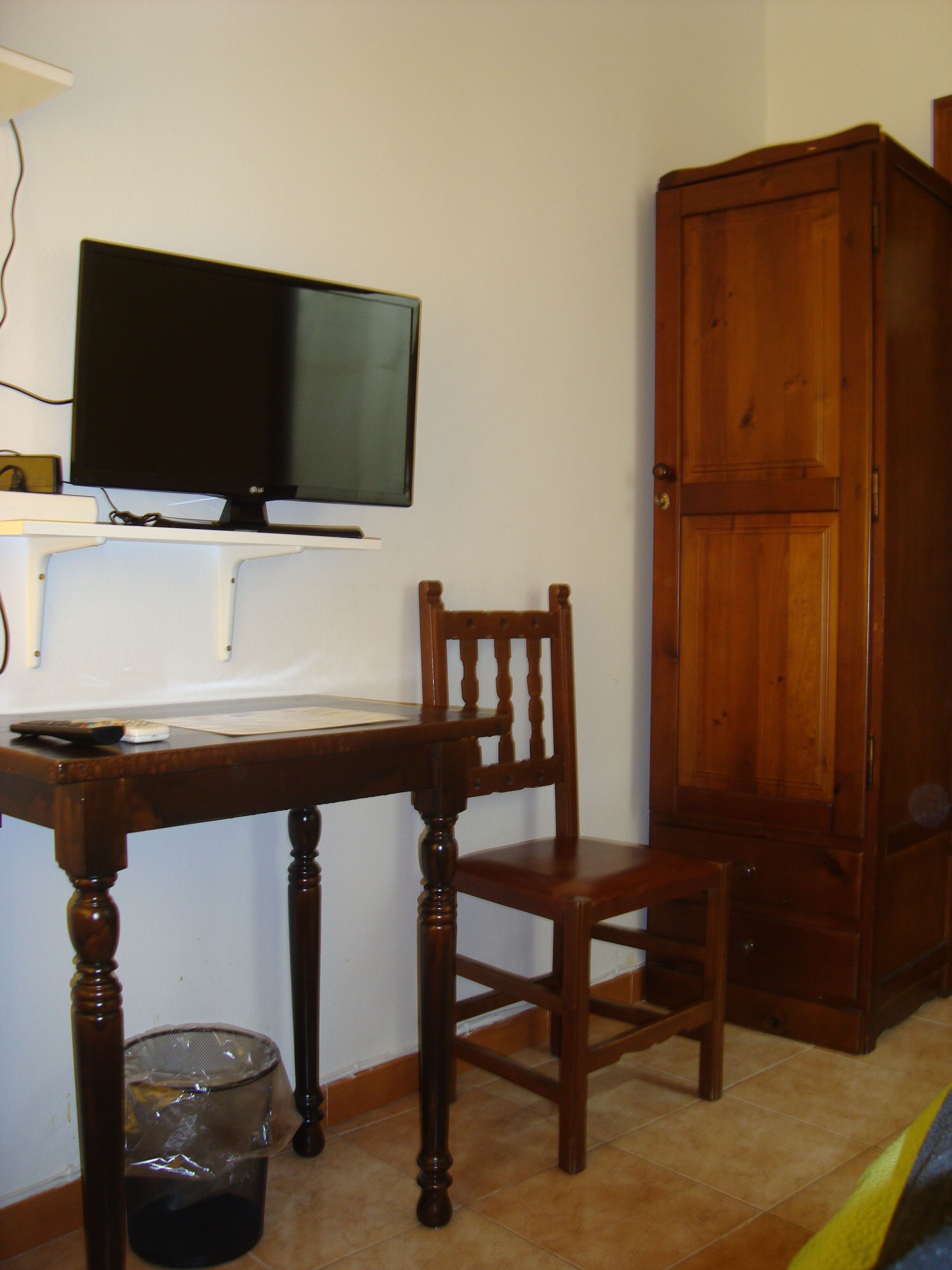 A room with a wooden desk, a chair, a television, and a wooden wardrobe.