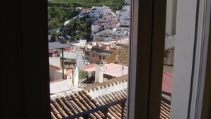 A balcony with terracotta tiles and a view of a town with white buildings and a hill with a tower. - Hostal Durán (Álora)