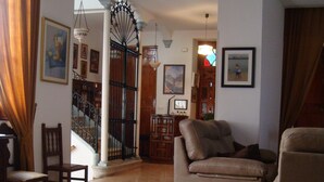 A living room with a glass-top coffee table, a sofa, a chair, and a staircase with a wrought iron railing. - Hostal Durán (Álora)