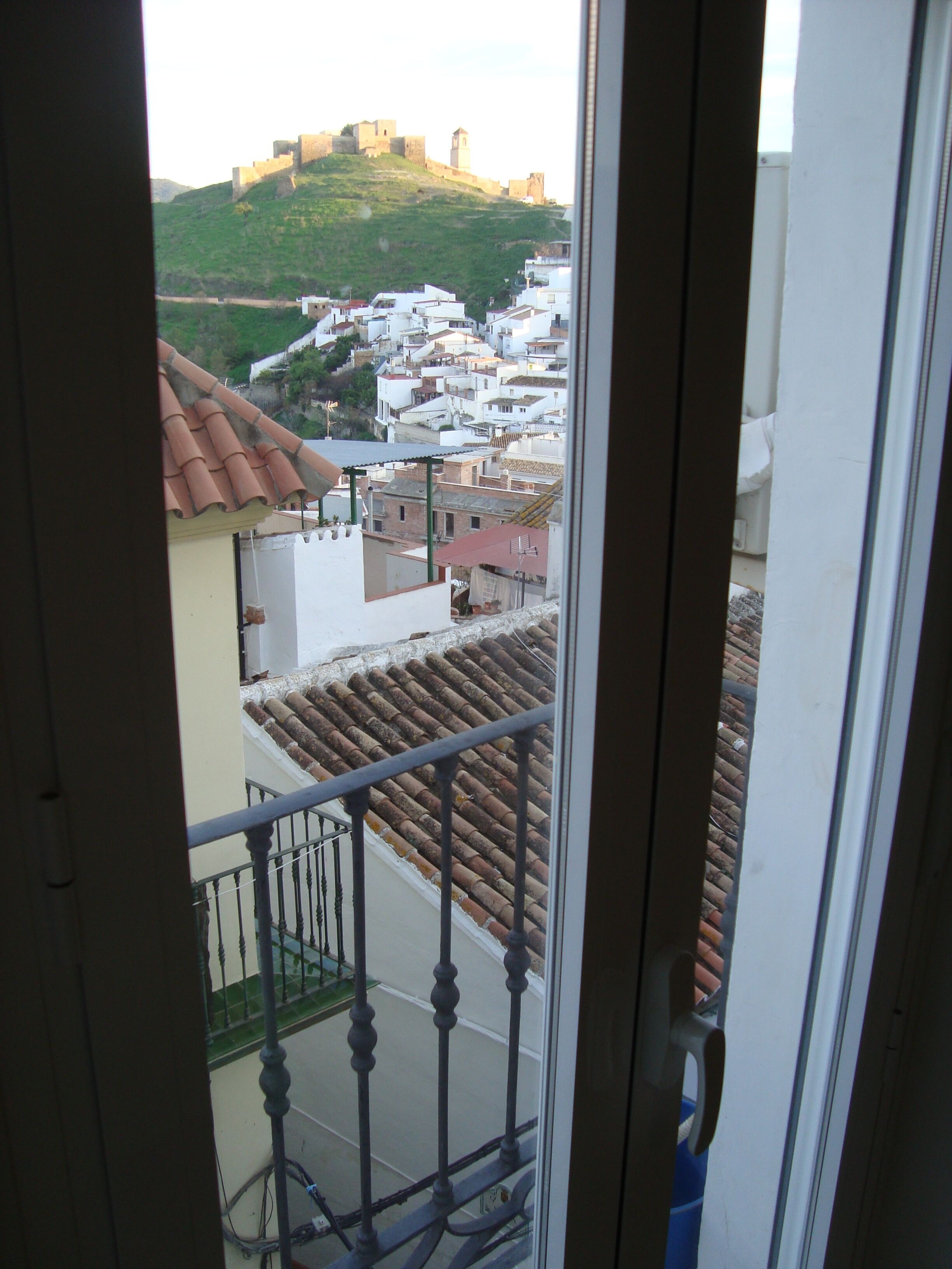 Un balcón con vistas a un pueblo, incluyendo una colina con una construcción similar a un castillo.