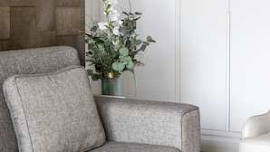 Una sala de estar moderna con un sofá gris, una mesita con un objeto decorativo, un jarrón con flores y un cuadro en la pared.