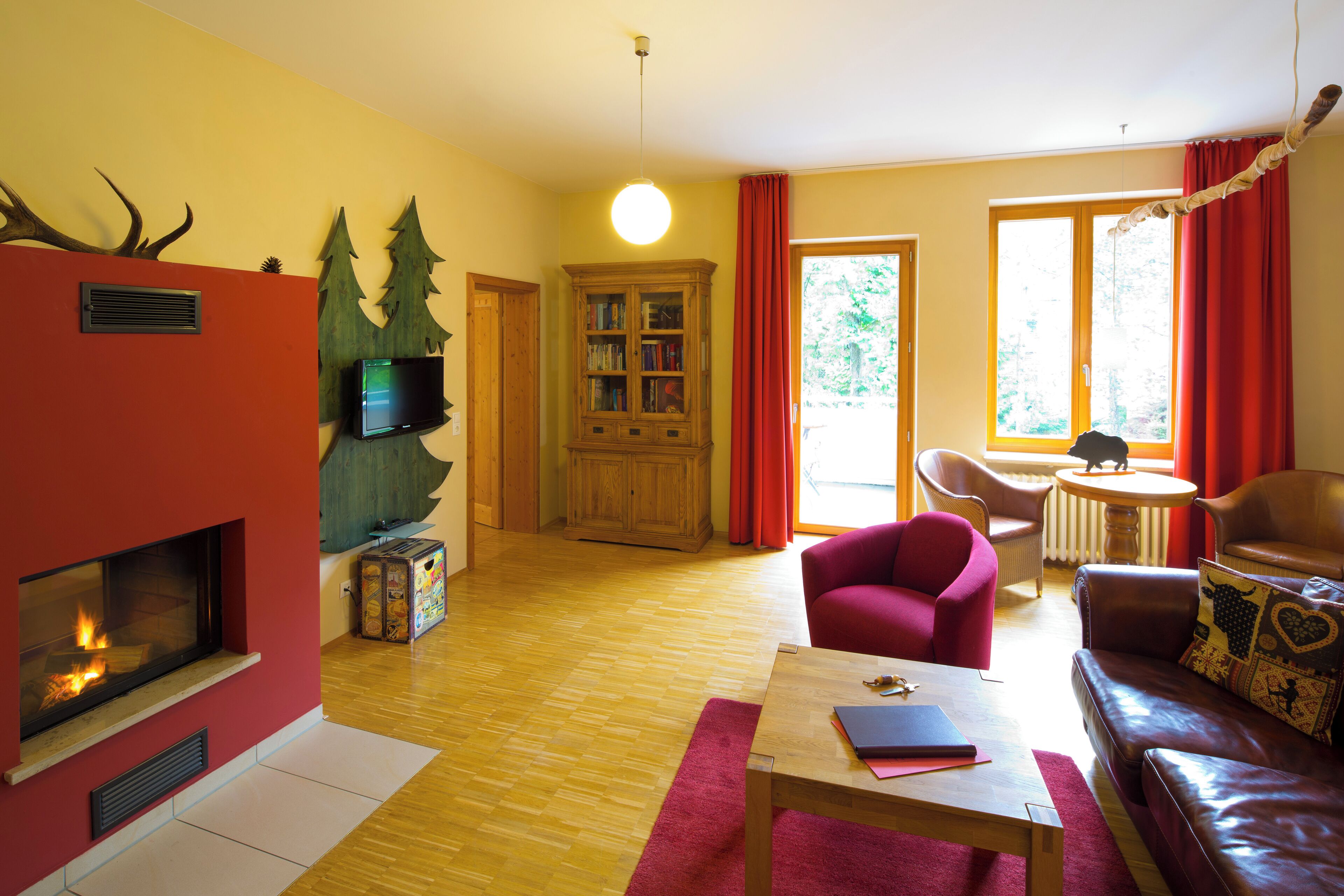 A living room with a fireplace, a wooden cabinet, a red armchair, a brown leather sofa, and a dining area with a table and chairs.