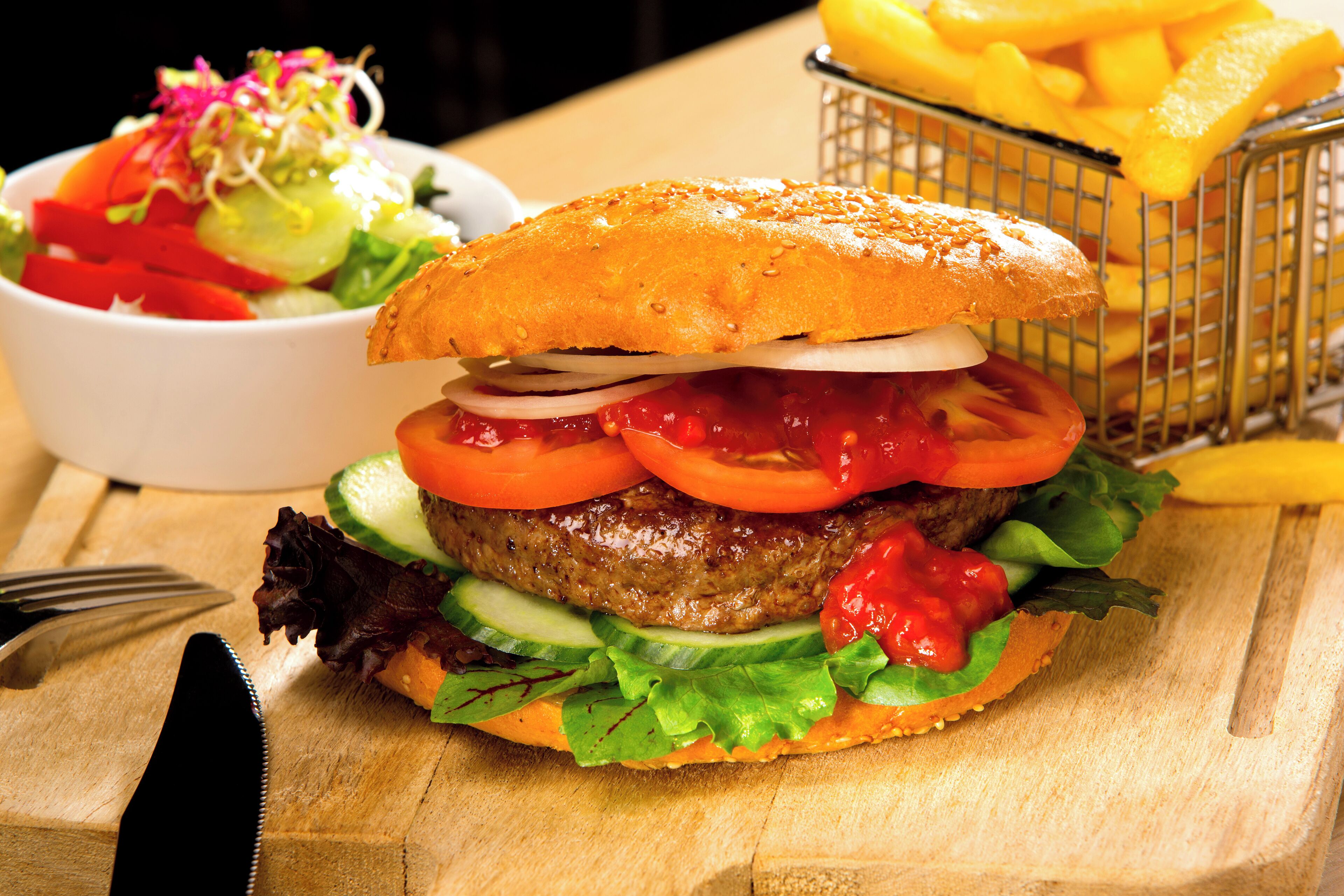 Un hamburger garni de laitue, de tomate et d’oignon, accompagné d’une portion de frites, le tout servi sur une table en bois.