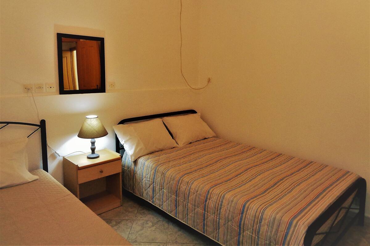 A small, single-bed room with a bedside table, a lamp, and a mirror on the wall.