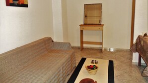 A living room with a sofa, a table with a bowl of fruit, and a painting on the wall. - Elena's House (Kalamata)