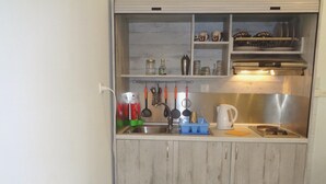 A compact kitchenette with a sink, stove, and storage shelves. - Elena's House (Kalamata)