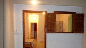 A hallway leading to a bedroom with a bed, a wooden door, and a small table. - Elena's House (Kalamata)