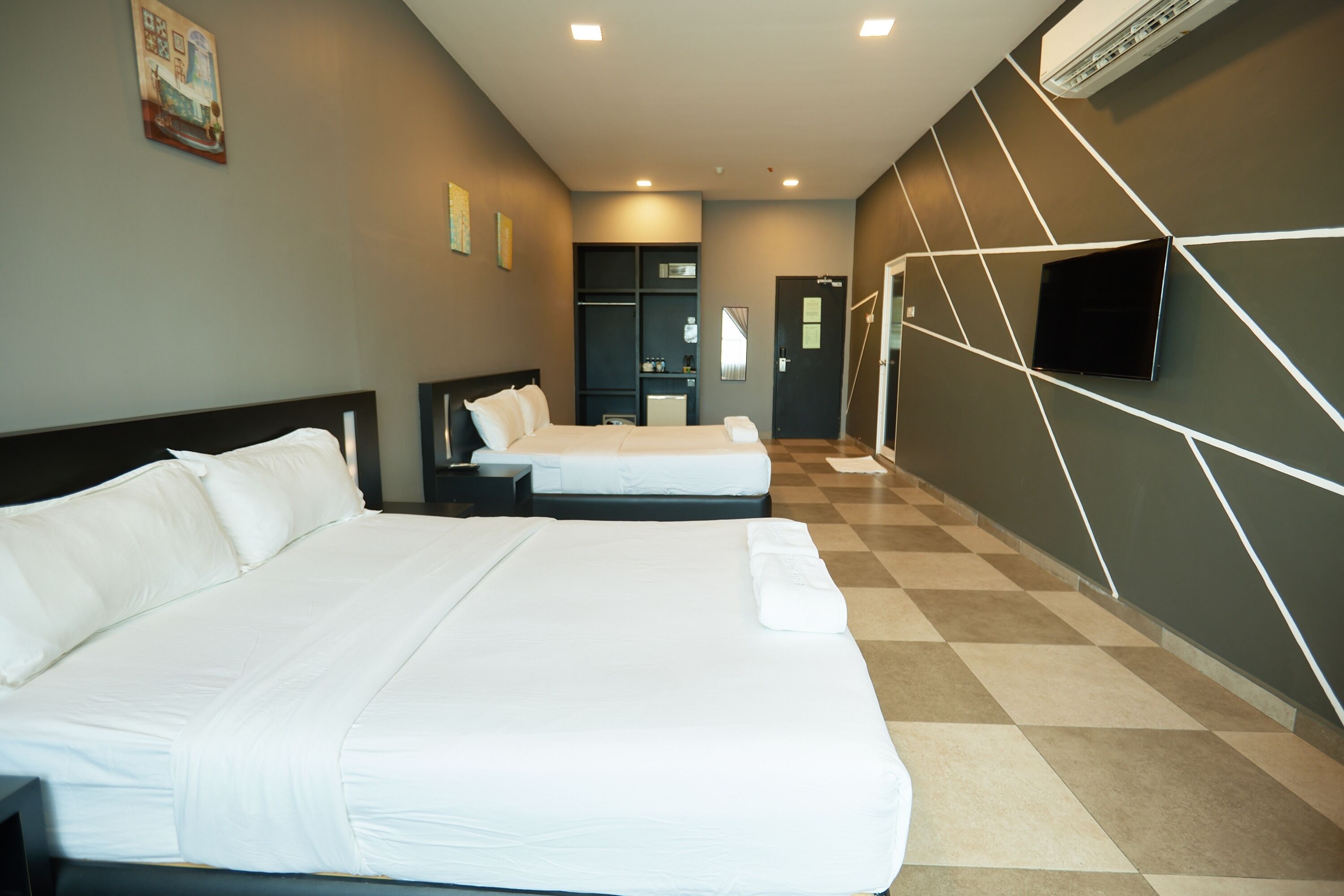 A hotel room with two beds, a flat-screen TV mounted on the wall, and a checkered floor.