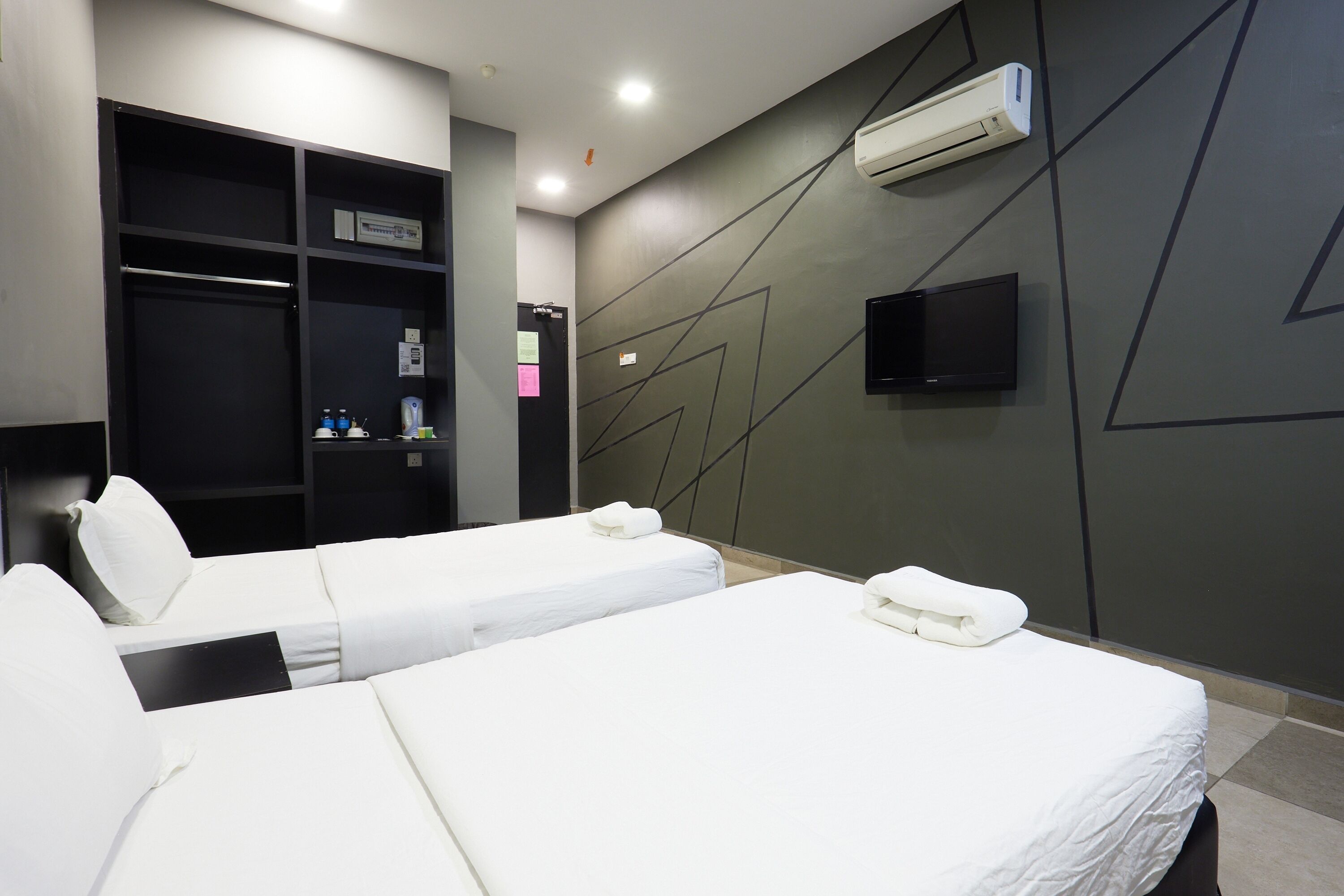 A hotel room with two beds, a wardrobe, a flat-screen TV, and an air conditioning unit.