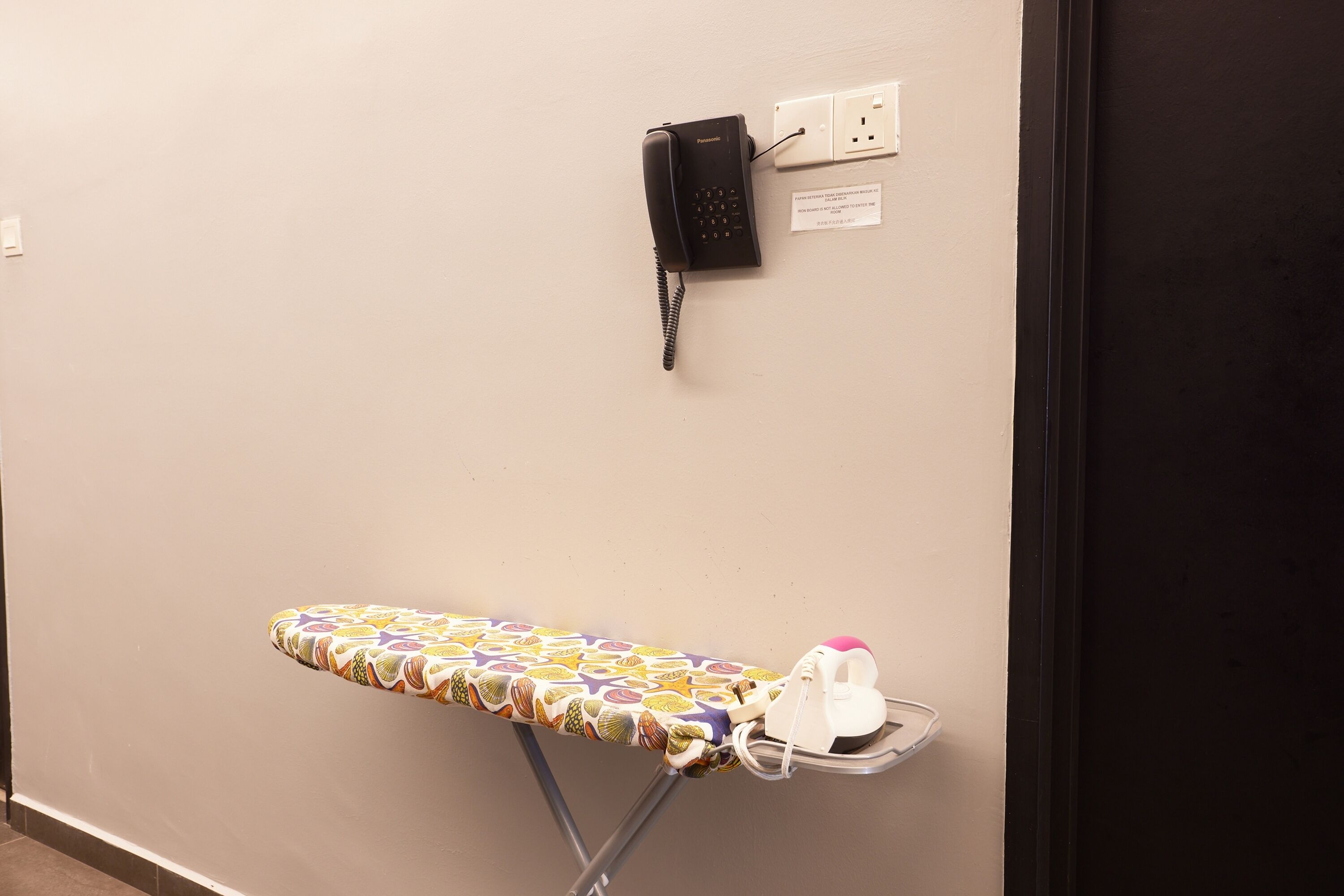 Una tabla de planchar fijada a la pared, un planchador y un teléfono.