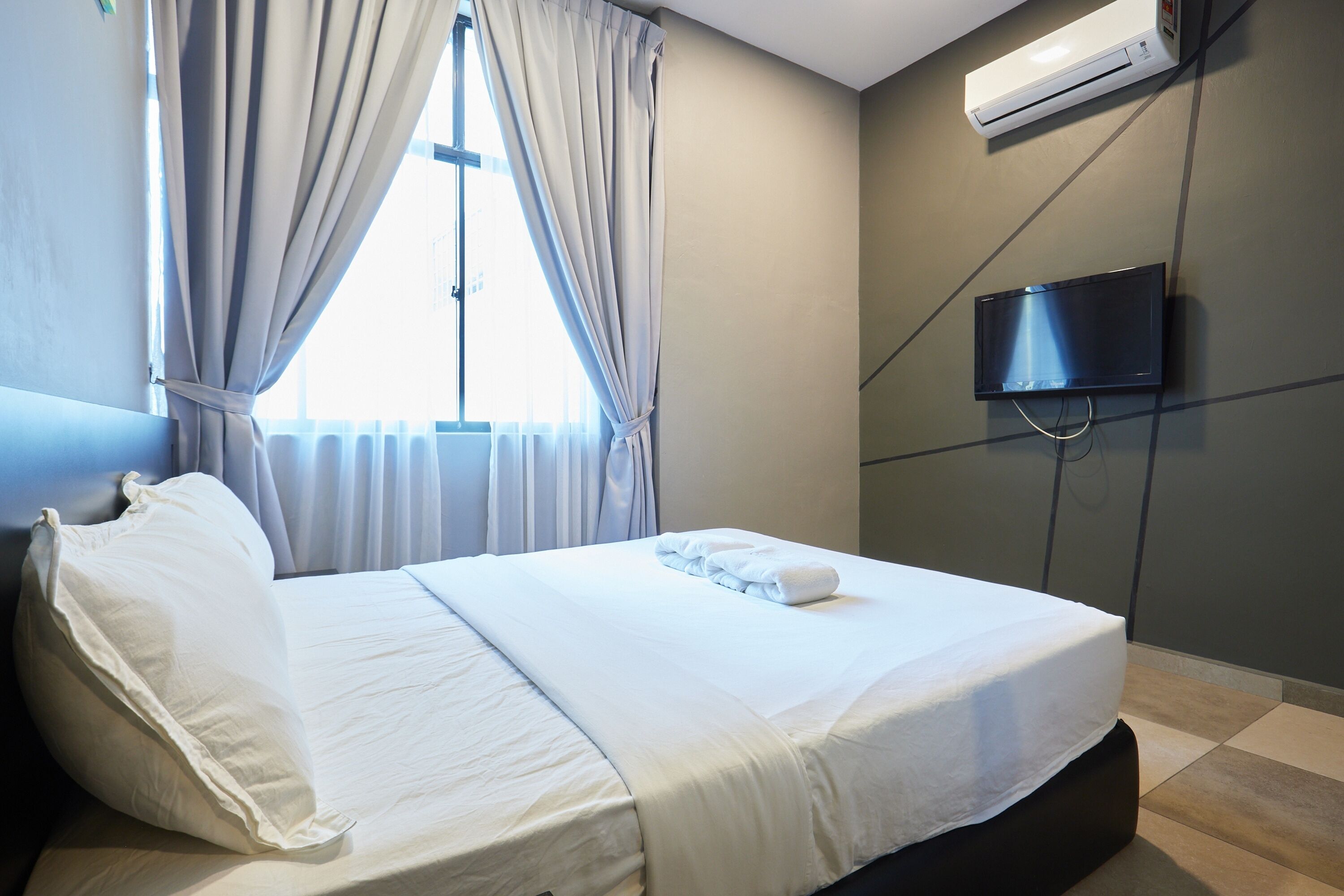 Una habitación de hotel con cama, cortinas, un equipo de aire acondicionado y una televisión.