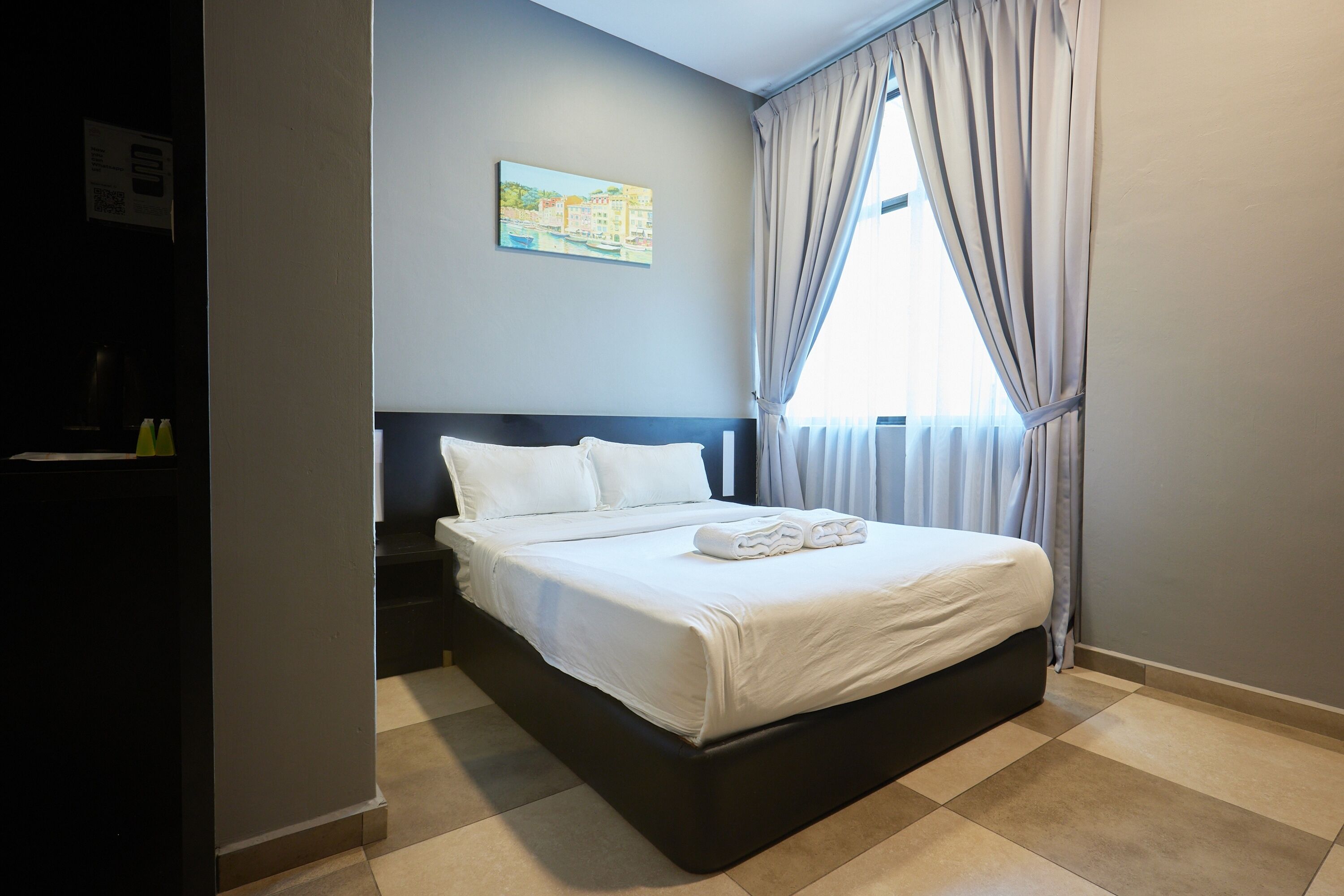 Een hotelkamer met een bed, een schilderij aan de muur en een raam met gordijnen.
