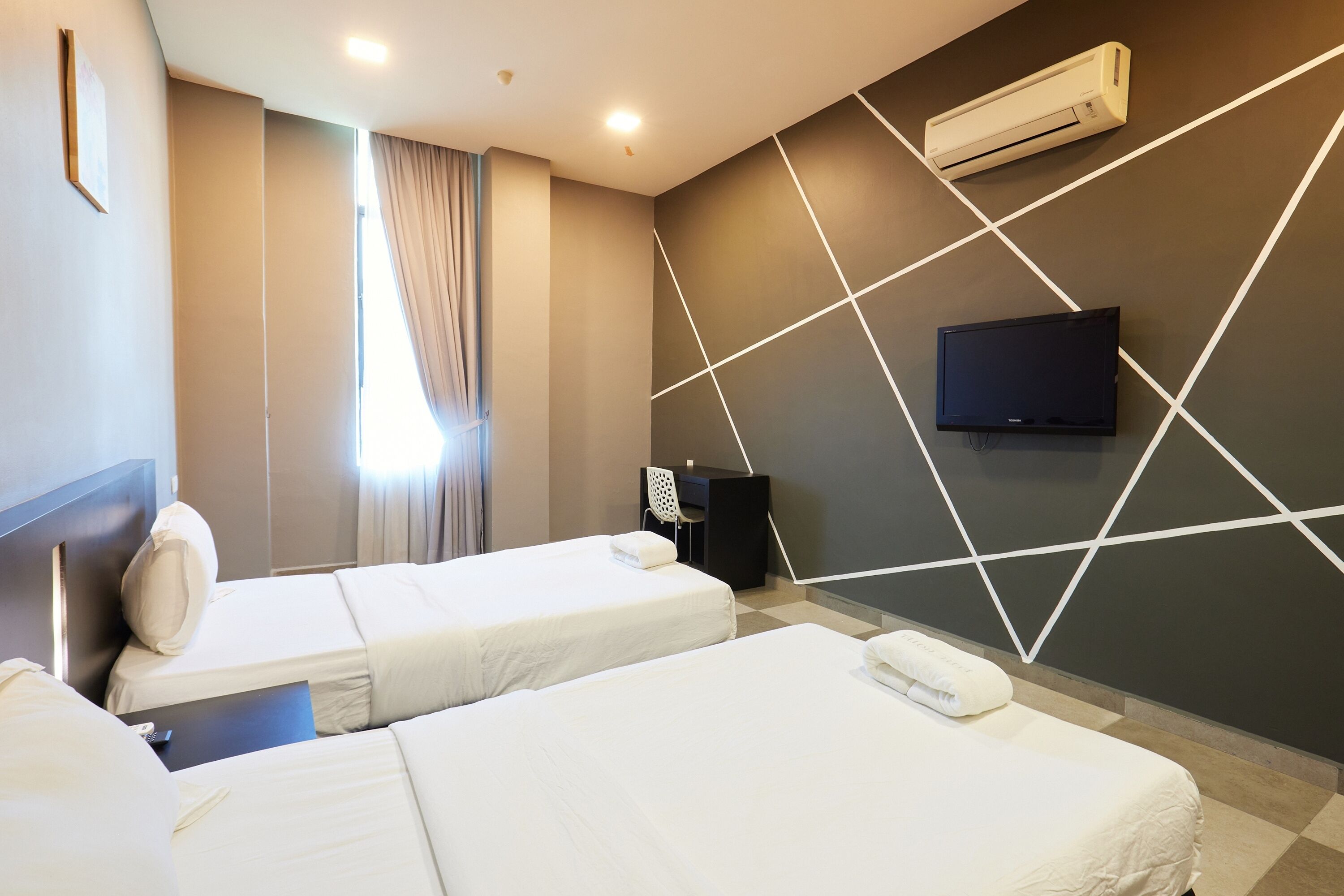 A hotel room with two beds, a flat-screen TV mounted on the wall, and an air conditioning unit.