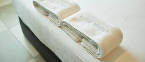 Una cama bien hecha con dos toallas dobladas encima, ambas con la etiqueta 'ELITE HOTEL'.