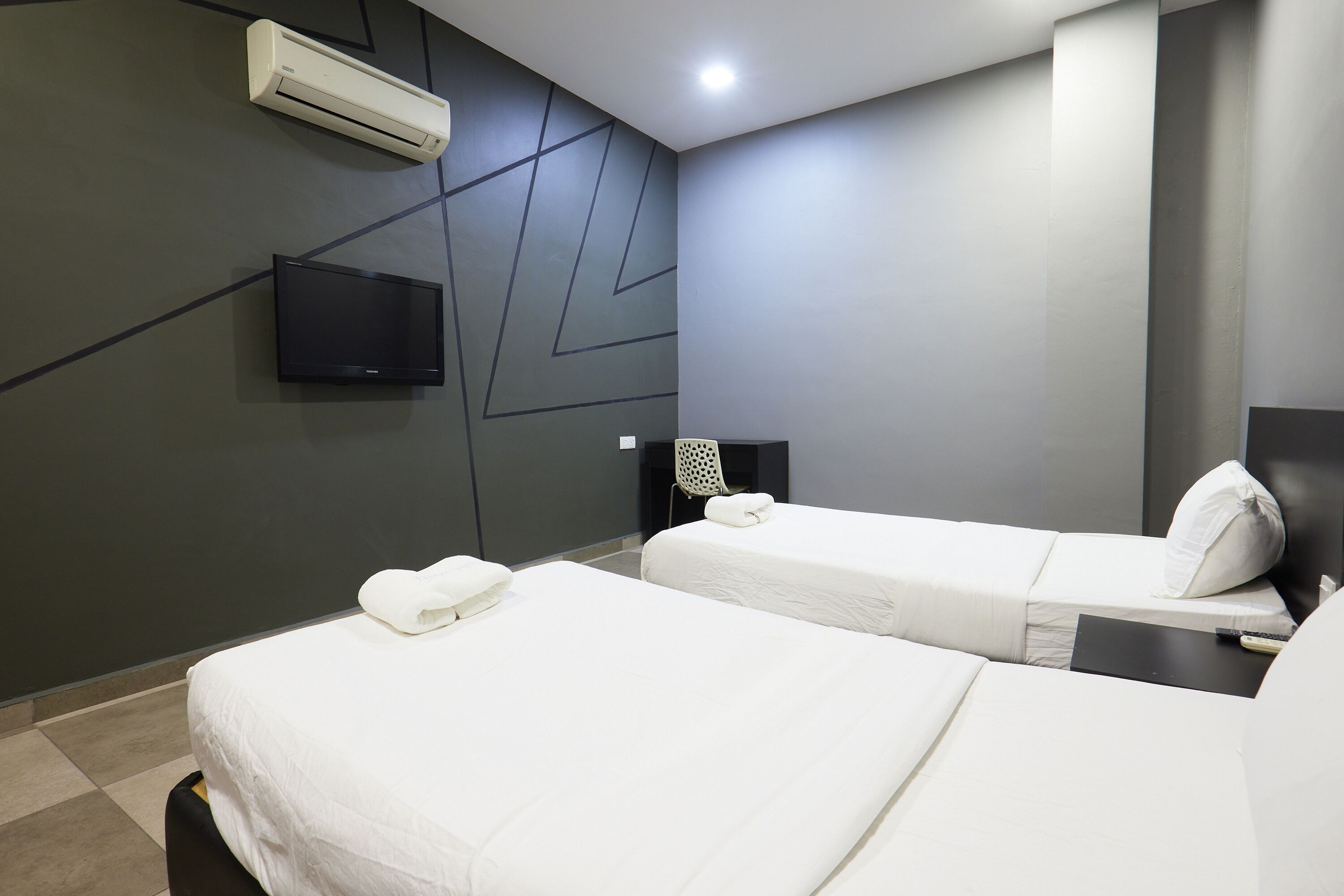Habitación de hotel con dos camas, un televisor de pantalla plana, aire acondicionado y un diseño moderno en la pared.