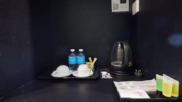 Minibar de una habitación de hotel con una bandeja que contiene dos vasos, dos botellas de agua, una jarra de cristal, una pequeña bandeja con una bolsita de té, una bolsita de té Lipton y varios sobres de té.