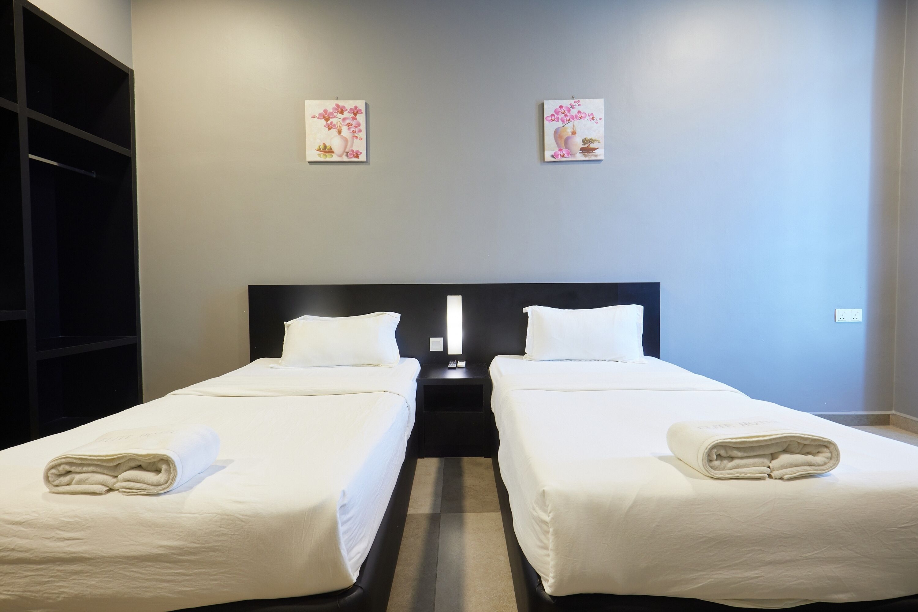 Une chambre d’hôtel avec deux lits simples, une grande armoire et deux tableaux accrochés au mur.