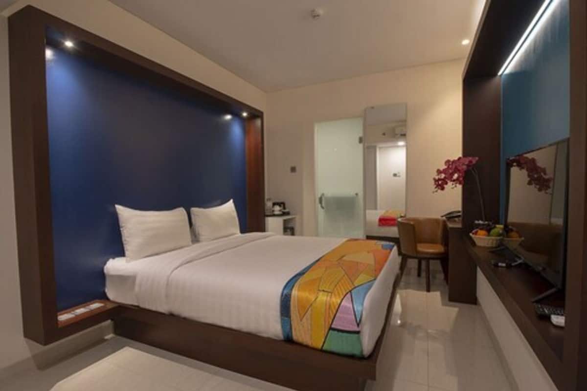 Ein modernes Hotelzimmer mit einem großen Bett, einem Schreibtisch mit Stuhl, einem Spiegel und einem kleinen Tisch mit Obst.