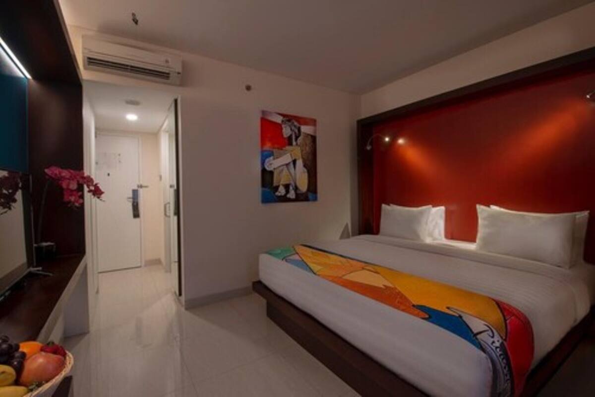 A hotel room with a bed, a painting on the wall, and a hallway leading to another room.