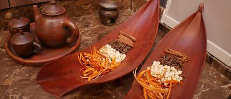 A kitchen with a marble countertop, a clay teapot, a clay pot, and two wooden boats containing spices and nuts.