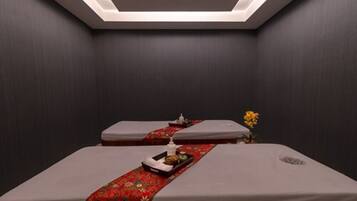 Un cuarto de spa con dos camillas de masaje, una bandeja con aperitivos y una pequeña planta decorativa.