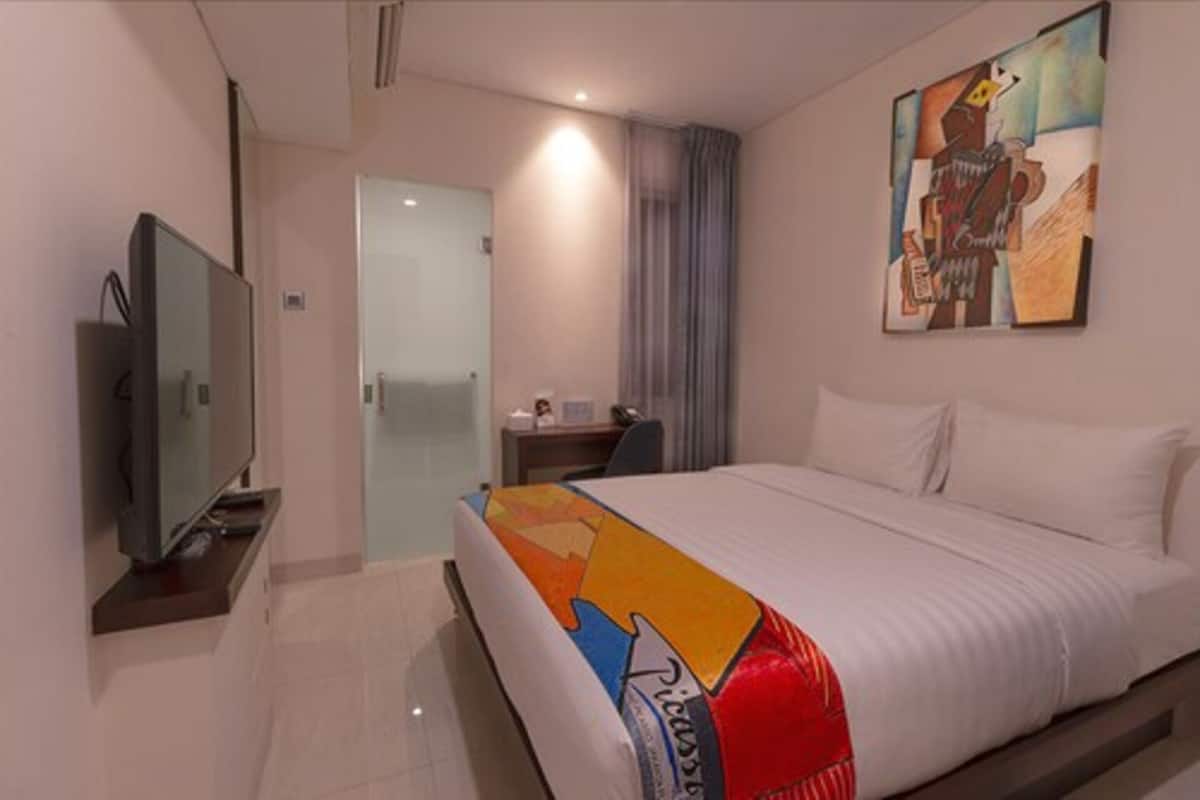 A hotel room with a bed, a television, a desk, and a painting on the wall.