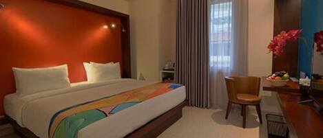 A hotel room with a large bed, a wooden headboard, a desk with a chair, and a window with curtains.