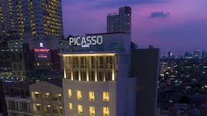 A modern hotel with a prominent 'PICASSO HOTEL' sign, multiple balconies, and a well-lit facade. - Grand Picasso Hotel (Jakarta)