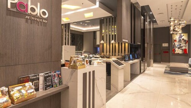 A modern interior with a reception desk, a display of timepieces, and a clean, polished floor. - Grand Picasso Hotel (Jakarta)